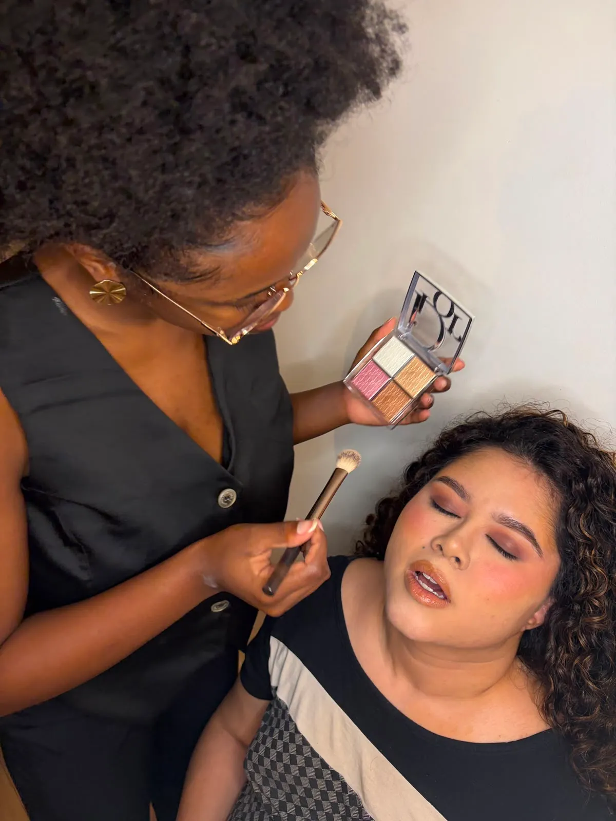 Laura aplicando maquiagem com pincel e paleta durante atendimento a domicílio